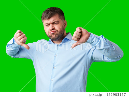 Man expressing disapproval with thumbs down gesture against a bright green background Man expressing disapproval with thumbs down gesture against a bright green background 122903157