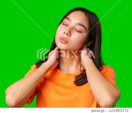 Young woman with closed eyes showing relaxation while holding her neck in a bright orange shirt against a green background Young woman with closed eyes showing relaxation while holding her neck in a bright orange shirt against a green background 122903172