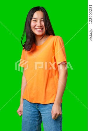 Smiling young woman in bright orange shirt on green background shows enthusiasm and joy while posing Smiling young woman in bright orange shirt on green background shows enthusiasm and joy while posing 122903281
