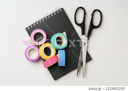 Crafting essentials on a workspace featuring colorful tape and scissors beside a notepad 122903295