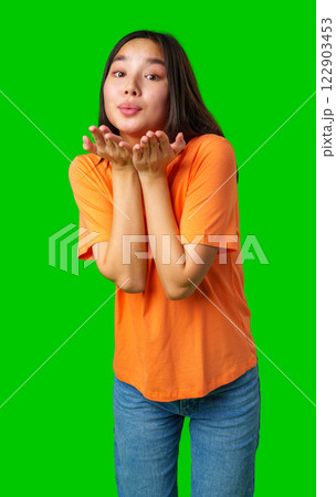 Cheerful young woman in orange shirt blowing kisses on bright green background during daylight Cheerful young woman in orange shirt blowing kisses on bright green background during daylight 122903453