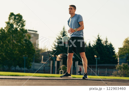 Young man prepares for soccer practice on a sunny day in a city park with green grass and trees 122903460