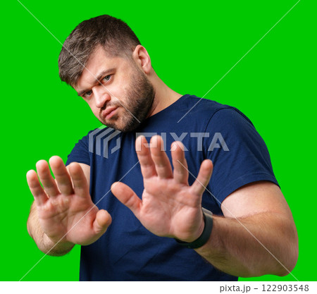 A man with a serious expression holds up both hands in a stopping gesture against a bright green background A man with a serious expression holds up both hands in a stopping gesture against a bright green background 122903548