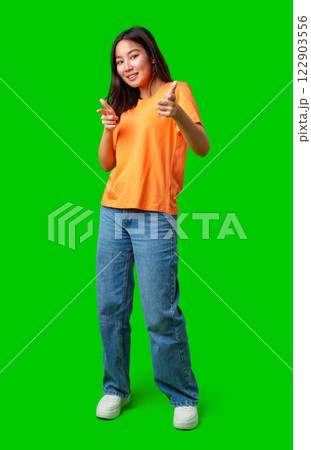 Young woman poses playfully in orange shirt and jeans against bright green background Young woman poses playfully in orange shirt and jeans against bright green background 122903556