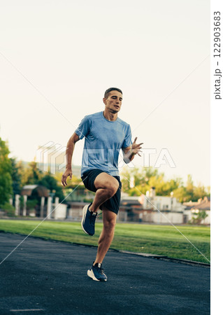 Runner practicing high knees on a track under clear skies in early morning 122903683