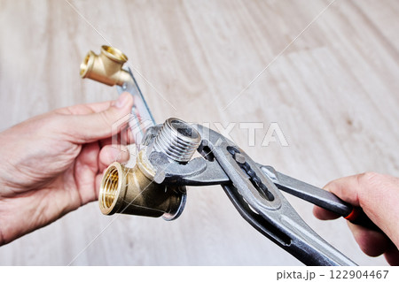 Wrench is tightening stainless steel threaded nipple wrapped in plumbing flax into brass fitting for secure plumbing installation. 122904467