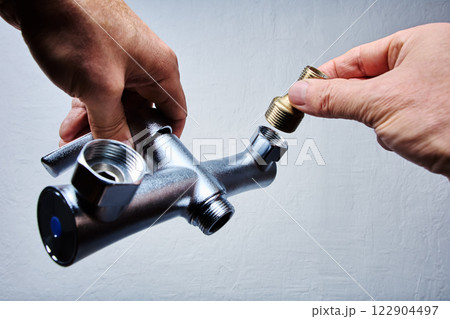Hands attach brass eccentric reducer to plumbing fixture of . bathroom mixer tap with threaded connectors. Hands attach brass eccentric reducer to plumbing fixture of . bathroom mixer tap with threaded connectors. 122904497