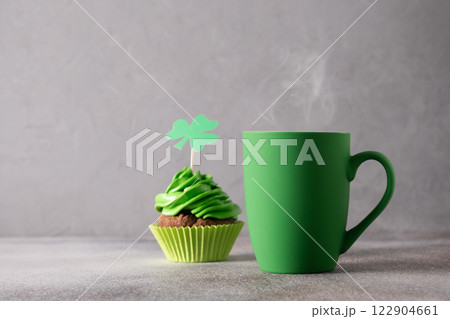St. Patrick's Day food. Irish coffee in green cup and chocolate cupcake decorated whipped green cream and traditional symbol shamrock on gray background. Close up. 122904661