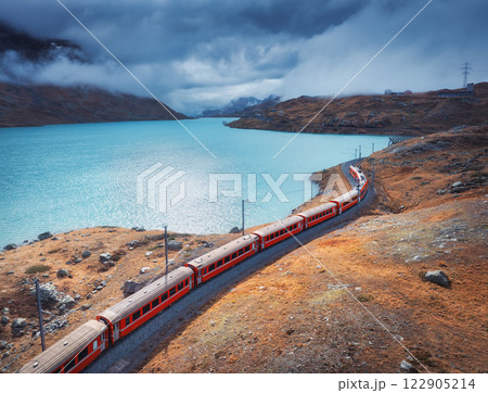 Aerial view of red train near alpine mountain lake and cloudy sky 122905214