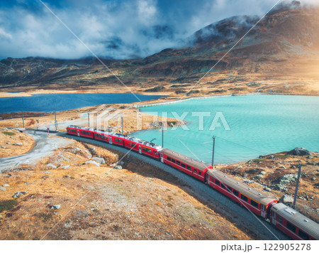 Aerial view of red train near alpine mountain lake and cloudy sky Aerial view of red train near alpine mountain lake and cloudy sky 122905278