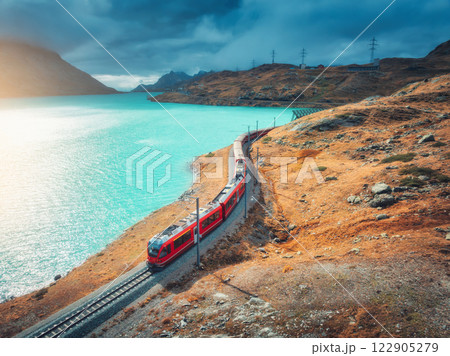 Aerial view of red train near alpine mountain lake and cloudy sky 122905279