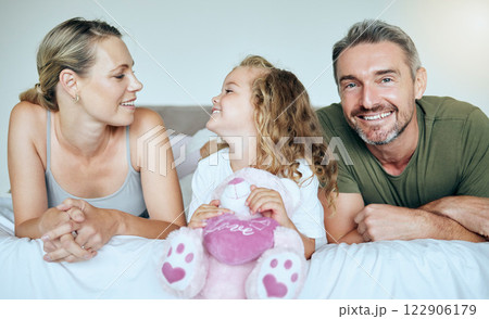 Happy, smile and family relaxing on a bed while bonding in their calm and comfortable bedroom. Happiness, love and care between parents and a girl child holding a teddy while resting in a modern home 122906179
