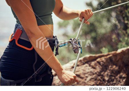 Fitness, safety and hands of rock climbing woman with security, harness cable or sport equipment on mountain cliff. Travel, hiking or adventure girl exercise with mountaineering rope workout training 122906240