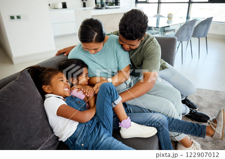 Happy, laugh and play family smile in the lounge at home. Mother, father and young children playing, having fun and bonding. Parents teasing, joking and tickling their adorable and cute kids 122907012