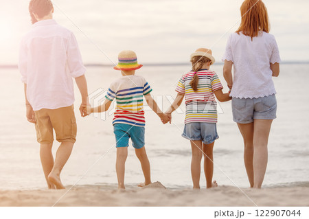 A family stands by holding hands on the seashore at the water's edge looking into the distance. 122907044