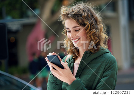 Happy woman, smile and typing on phone during travel in city using social media, internet and 5g network connection outside. Young female flirting on a mobile app for communication on urban street 122907235