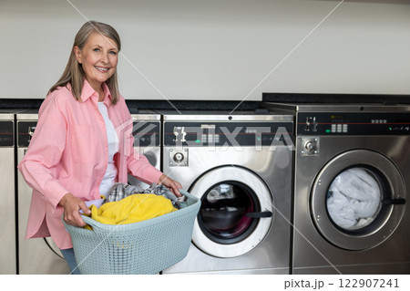Smiling mature caucasian woman in pink tshirt carrying a basket with clean clothes from laundry Smiling mature caucasian woman in pink tshirt carrying a basket with clean clothes from laundry 122907241