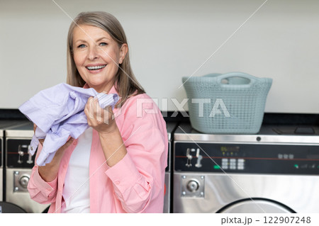 Mature caucasian woman in pink tshirt holding in hands fresh clean clothes Mature caucasian woman in pink tshirt holding in hands fresh clean clothes 122907248
