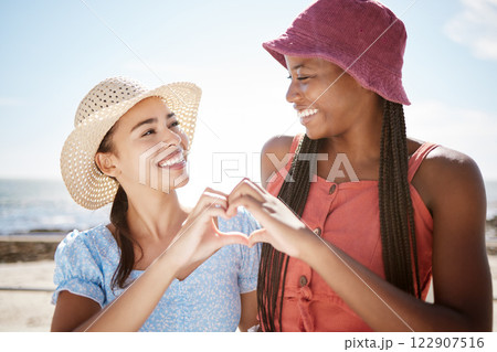 Happy interracial friends, smile and heart hand sign for love, beach and outdoor freedom together on summer vacation. Women couple in loving shape gesture for friendship happiness and joy on holiday Happy interracial friends, smile and heart hand sign for love, beach and outdoor freedom together on summer vacation. Women couple in loving shape gesture for friendship happiness and joy on holiday 122907516