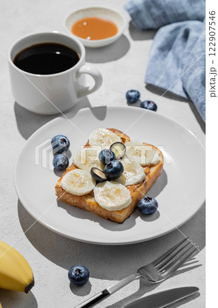 Peanut butter toast with banana and blueberry on a plate on a light background Peanut butter toast with banana and blueberry on a plate on a light background 122907546