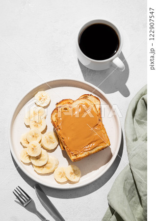 Peanut butter toast on a plate with banana on a light background with a cup of freshly brewed coffee Peanut butter toast on a plate with banana on a light background with a cup of freshly brewed coffee 122907547