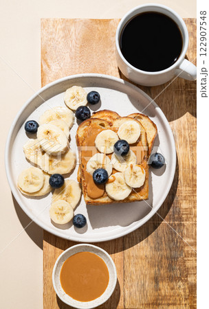 Peanut butter toast with banana and blueberry on a wooden board with a cup of freshly brewed coffee Peanut butter toast with banana and blueberry on a wooden board with a cup of freshly brewed coffee 122907548
