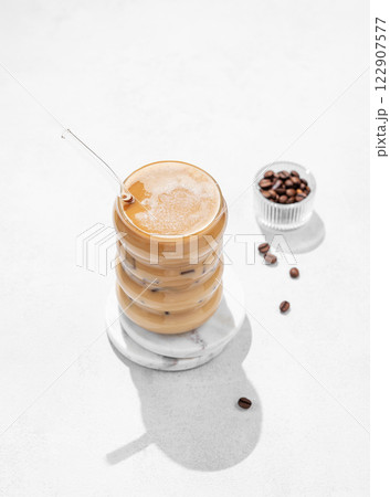Cold coffee latte or mocha in a glass with milk and ice on a light background with coffee beans Cold coffee latte or mocha in a glass with milk and ice on a light background with coffee beans 122907577