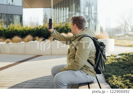 Portrait handsome young man taking selfie on urban background. 30s man using phone outdoors. Smiling businessman walking in urban area. Urban lifestyle concept. Spring time. Portrait handsome young man taking selfie on urban background. 30s man using phone outdoors. Smiling businessman walking in urban area. Urban lifestyle concept. Spring time. 122908892