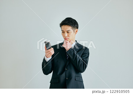 あごに手を当ててスマホを持つ20代の若い男性 あごに手を当ててスマホを持つ20代の若い男性 122910505