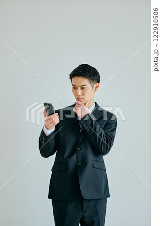 あごに手を当ててスマホを持つ20代の若い男性 122910506