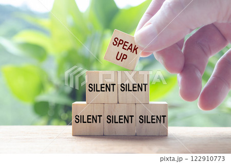 Hand putting Speak Up wooden cube on top of other Silent cubes. Speak up culture concept 122910773