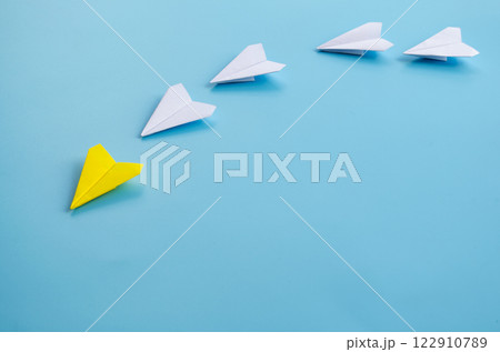 Side view of yellow paper airplane origami leading other white airplanes on blue background with customizable space for text. Business and Leadership skills concept. 122910789