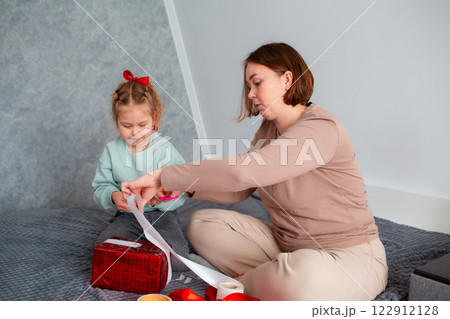 Mid shot of mother and daughter together packing a Valentine's Day and Mother's day gift. Family sitting on bed 122912128