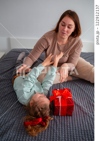 Vertical orientation of young Caucasian woman lies with her daughter. The girl prepared a gift for her mother for the holiday. The concept of family time Vertical orientation of young Caucasian woman lies with her daughter. The girl prepared a gift for her mother for the holiday. The concept of family time 122912137