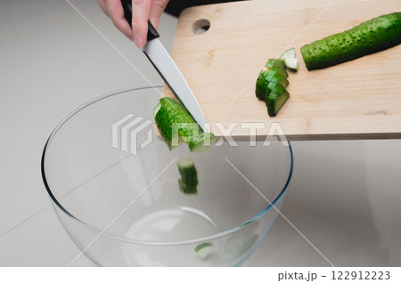 The photo shows slices of green cucumber cut on a board, a woman cutting a salad The photo shows slices of green cucumber cut on a board, a woman cutting a salad 122912223