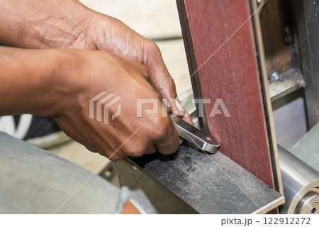 The hand deburring the metal parts with sandpaper belt by skill operator. The hand deburring the metal parts with sandpaper belt by skill operator. 122912272