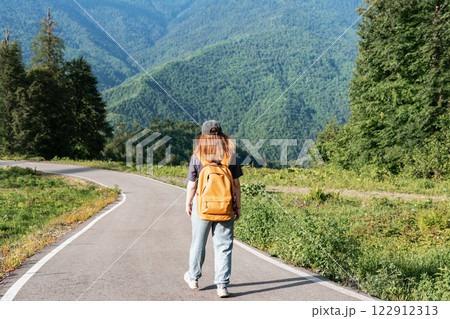 woman hiker in cap casual clothing with backpack walking along remote asphalt road with stunning view of green mountains Summer adventure and outdoor lifestyle , travel tourism concept woman hiker in cap casual clothing with backpack walking along remote asphalt road with stunning view of green mountains Summer adventure and outdoor lifestyle , travel tourism concept 122912313