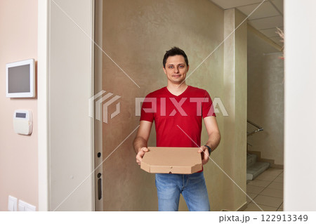 smiling delivery man in red t-shirt giving pizza box and standing at doorway 122913349
