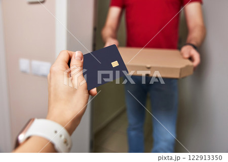 woman paying for pizza with black credit card at doorway, close-up 122913350