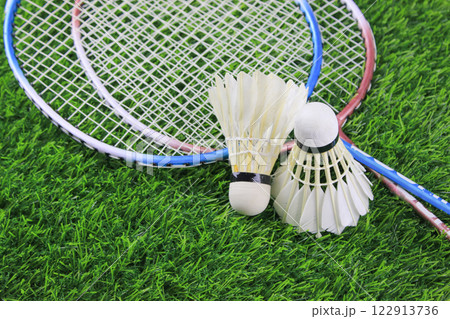 White shuttlecocks and badminton racket rest on artificial grass, outdoor sports and recreation. White shuttlecocks and badminton racket rest on artificial grass, outdoor sports and recreation. 122913736