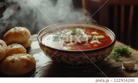 Russian Borscht bowl of soup with a dollop of sour cream on top sits on a wooden table. The bowl is filled with a hearty stew, and there are two rolls of bread nearby. Russian Borscht bowl of soup with a dollop of sour cream on top sits on a wooden table. The bowl is filled with a hearty stew, and there are two rolls of bread nearby. 122914200