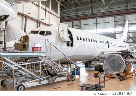 White passenger aircraft under maintenance has opened weather radar and engine removed located nearby in the airplane hangar White passenger aircraft under maintenance has opened weather radar and engine removed located nearby in the airplane hangar 122914464