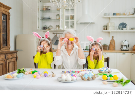 Happy Easter. Two little girls sisters twins grandmother painting eggs enjoying time together. Happy family grandma granddaughters child kids preparing for Easter. Spring Christian festival tradition Happy Easter. Two little girls sisters twins grandmother painting eggs enjoying time together. Happy family grandma granddaughters child kids preparing for Easter. Spring Christian festival tradition 122914727