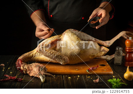 The chef seasons fresh turkey with dry aromatic herbs in a cozy kitchen setting. National dish from a large bird by the hands of the cook The chef seasons fresh turkey with dry aromatic herbs in a cozy kitchen setting. National dish from a large bird by the hands of the cook 122914755