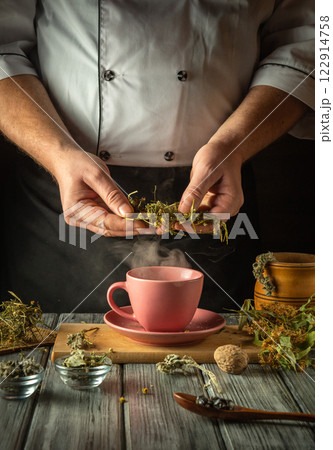 Experienced herbalist brews herbal tea. Hands holding dry medicinal chamomile to add to pink cup. Treatment of flu virus at home 122914758