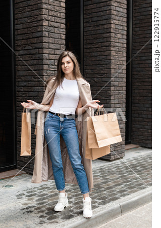 A girl in a casual clothes with shopping bags and lots of purchases near the shopping center smiling hands you her package, consumerism sale and people concept A girl in a casual clothes with shopping bags and lots of purchases near the shopping center smiling hands you her package, consumerism sale and people concept 122915774
