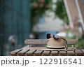 Stylish summer hat and dark glasses lie on a small textured table on a summer evening as a symbol of carefree vacation. 122916541