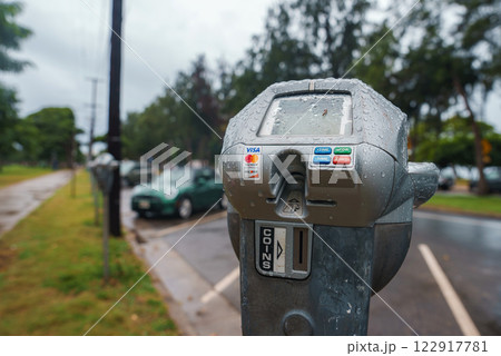 Modern parking meter with raindrops, coin and card payment options, wet pavement, parked cars, and a tree lined street in the background. Modern parking meter with raindrops, coin and card payment options, wet pavement, parked cars, and a tree lined street in the background. 122917781