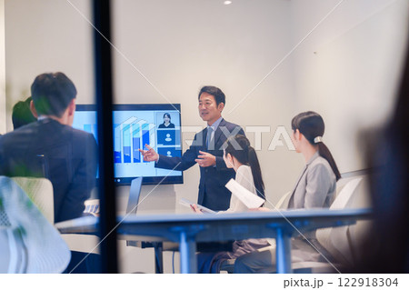 会議で資料を見ながらプレゼンをする中年のオフィスワーカー 122918304