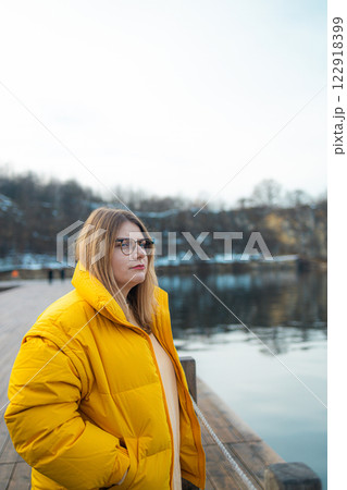 Young adult caucasian woman in yellow jacket breathing fresh air in the winter forest near a lake Young adult caucasian woman in yellow jacket breathing fresh air in the winter forest near a lake 122918399